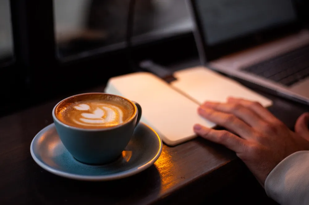 Latte beside a notebook and laptop at Licensed Coffee