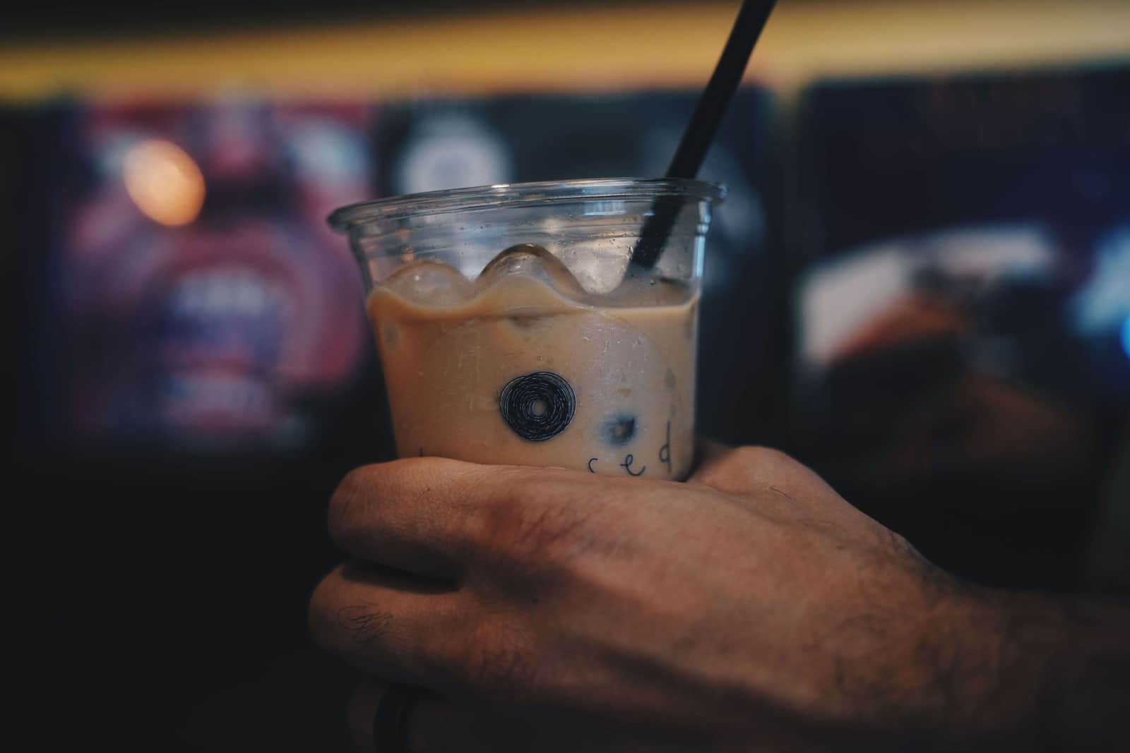 Vaso de café con hielo con el logo de Licensed Coffee delante de una pared de vinilos